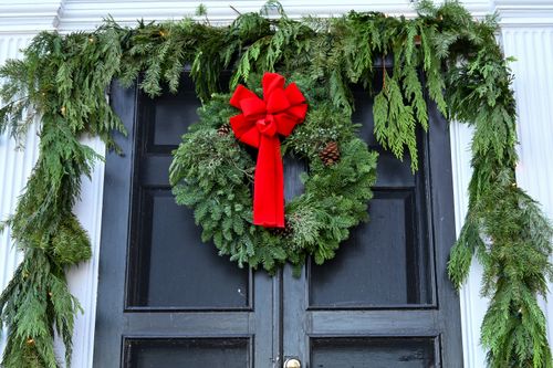 Free Elegant evergreen wreath with red bow adorns a classic black door in winter season. Stock Photo