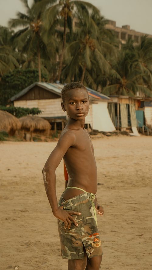 Free A young boy standing on a sandy tropical beach with palm trees at sunset. Stock Photo