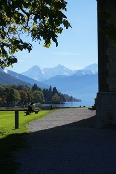 Beautiful view of Lake Thun with snowy mountains and serene park setting in Switzerland.