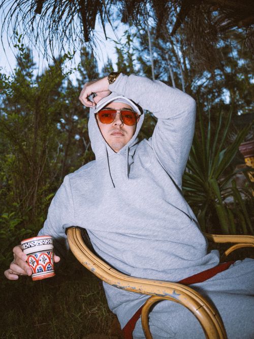 Free Young man in hoodie lounging outdoors with coffee and sunglasses. Stock Photo