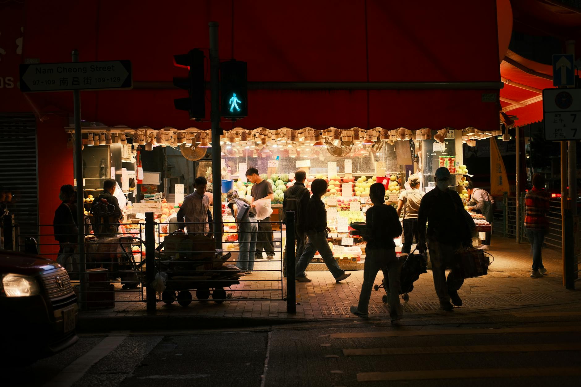 A vibrant night market scene in Hong Kong, with people shopping under a red canopy.