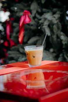 Glass of iced coffee on red table with Christmas tree backdrop.
