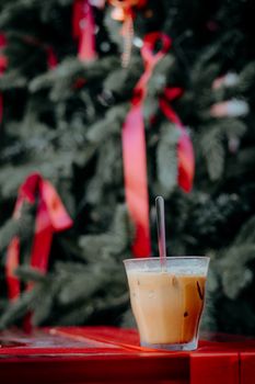 Iced coffee with a straw in front of a Christmas tree with red ribbons.