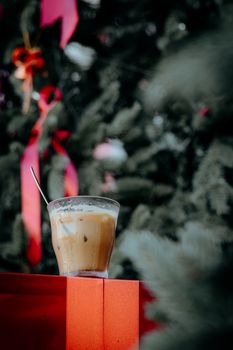 A glass of iced coffee in front of a decorated Christmas tree with red ribbons.