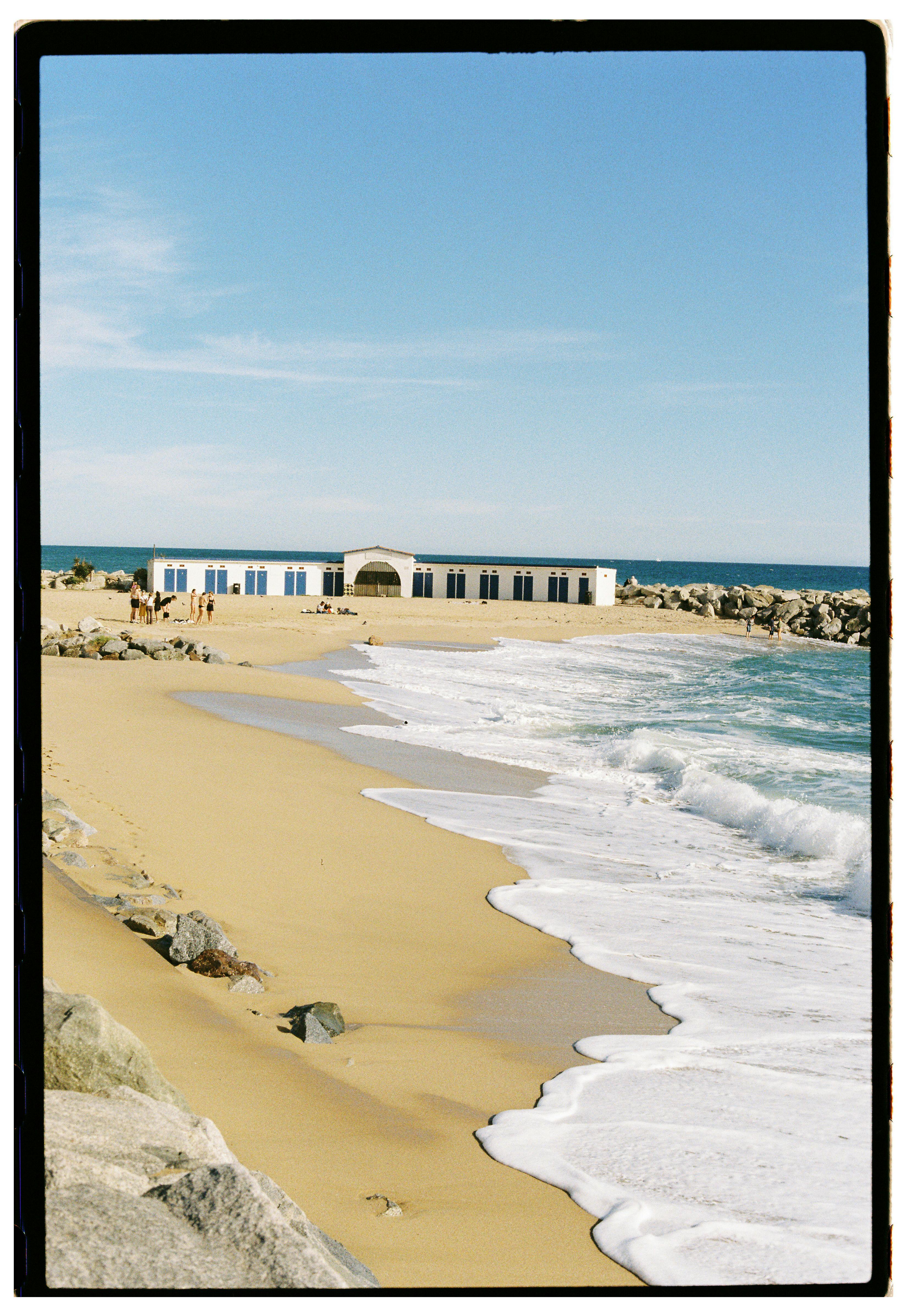 Scenic beach view with waves washing up on shore and a building in the distance.