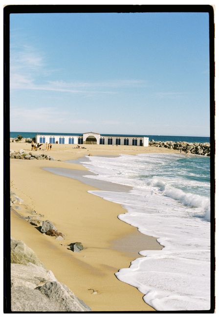 Scenic beach view with waves washing up on shore and a building in the distance.