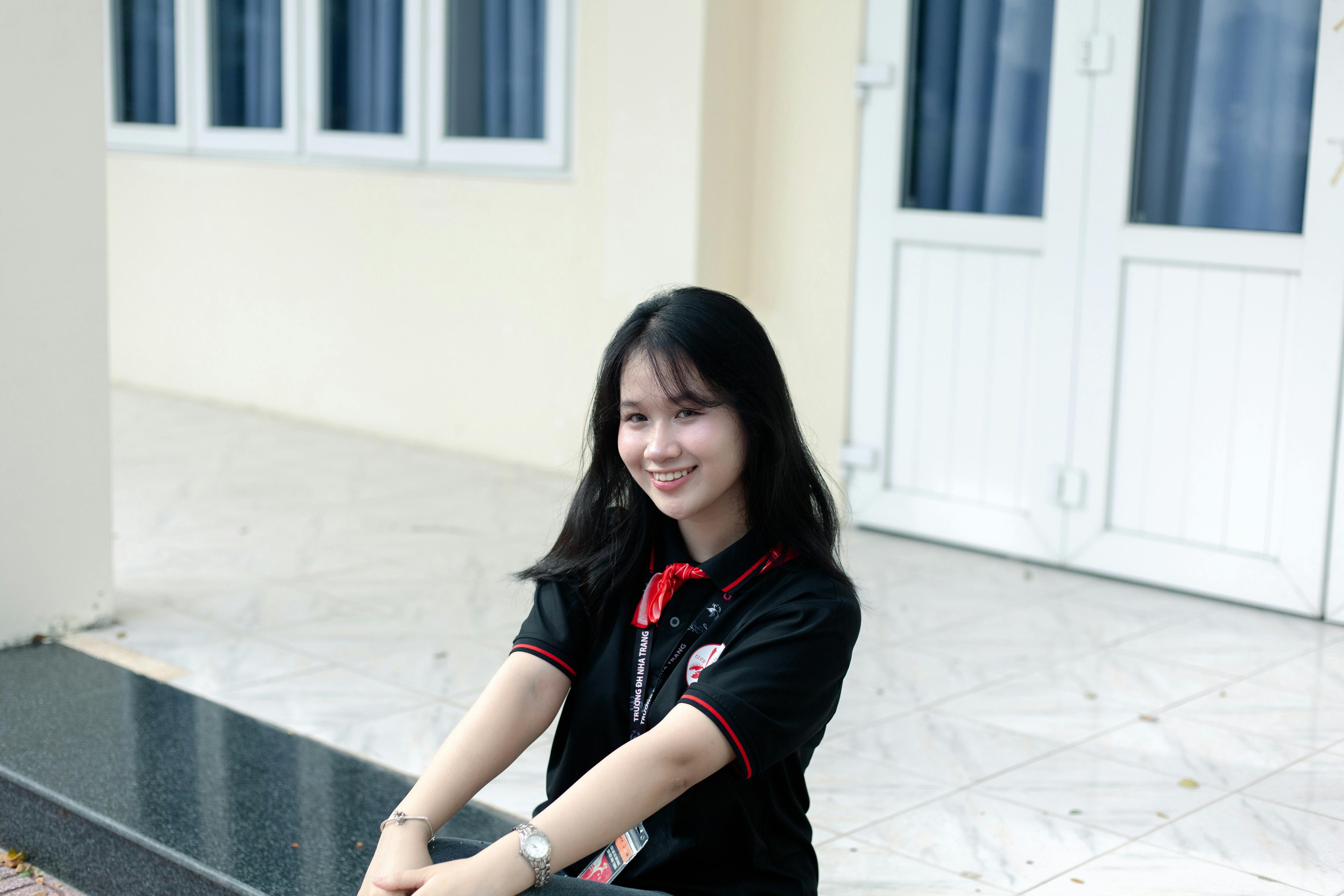 De franc Dona jove somrient asseguda fora d'un edifici blanc, amb un polo negre. Foto d'estoc