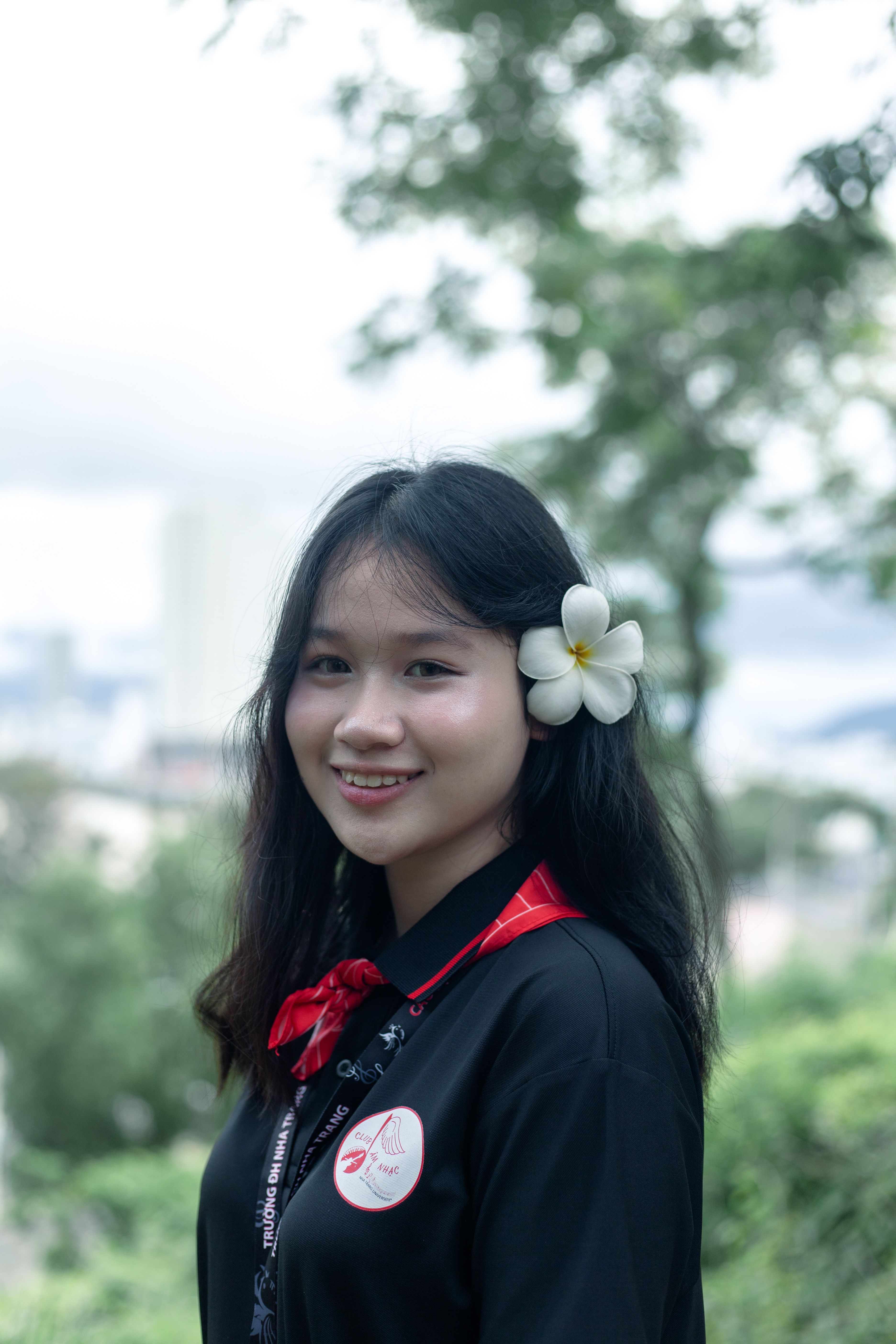 Young woman with a flower in her hair smiling in an outdoor setting. Vibrant and natural.