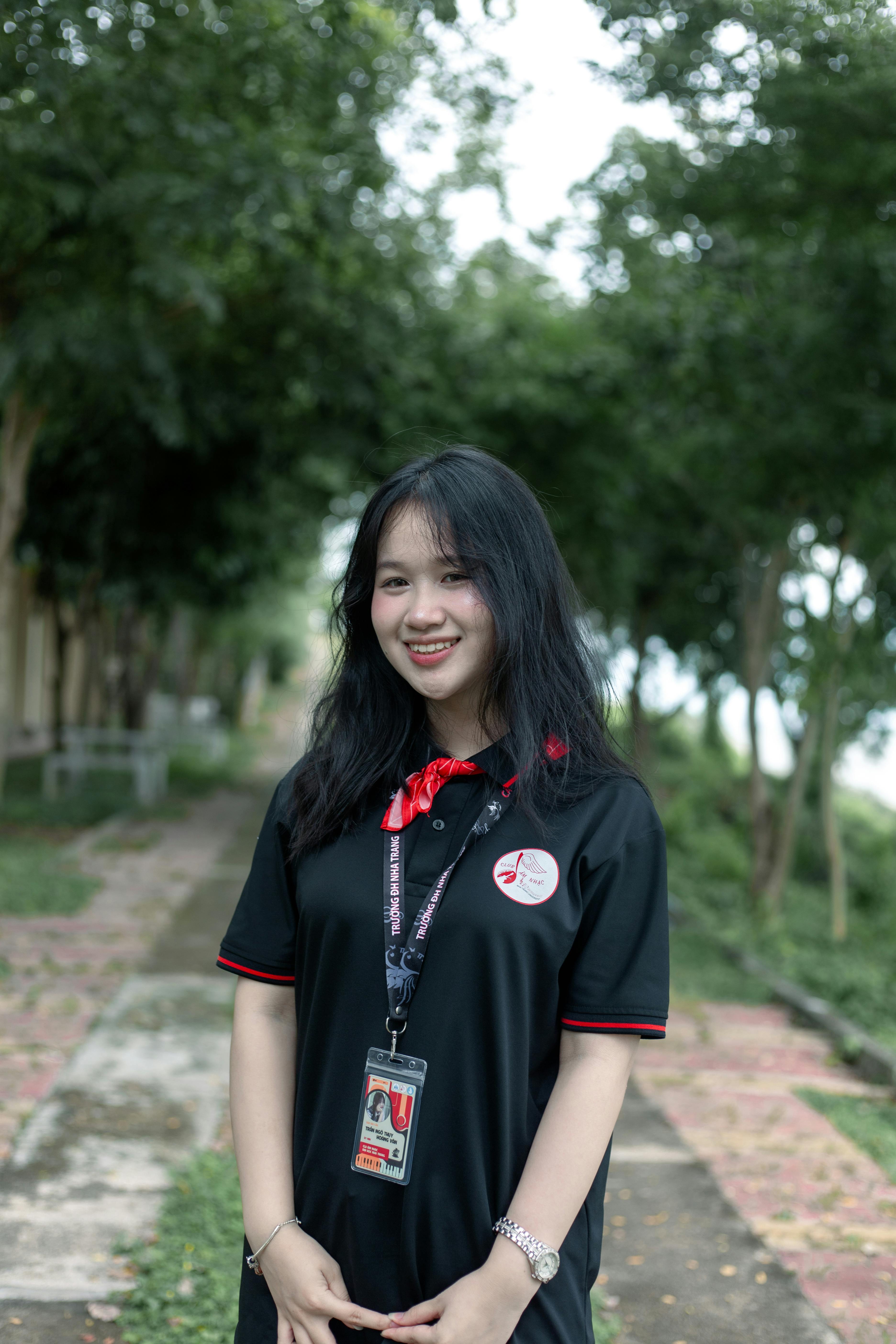 Young woman smiling outdoors on a tree-lined pathway.