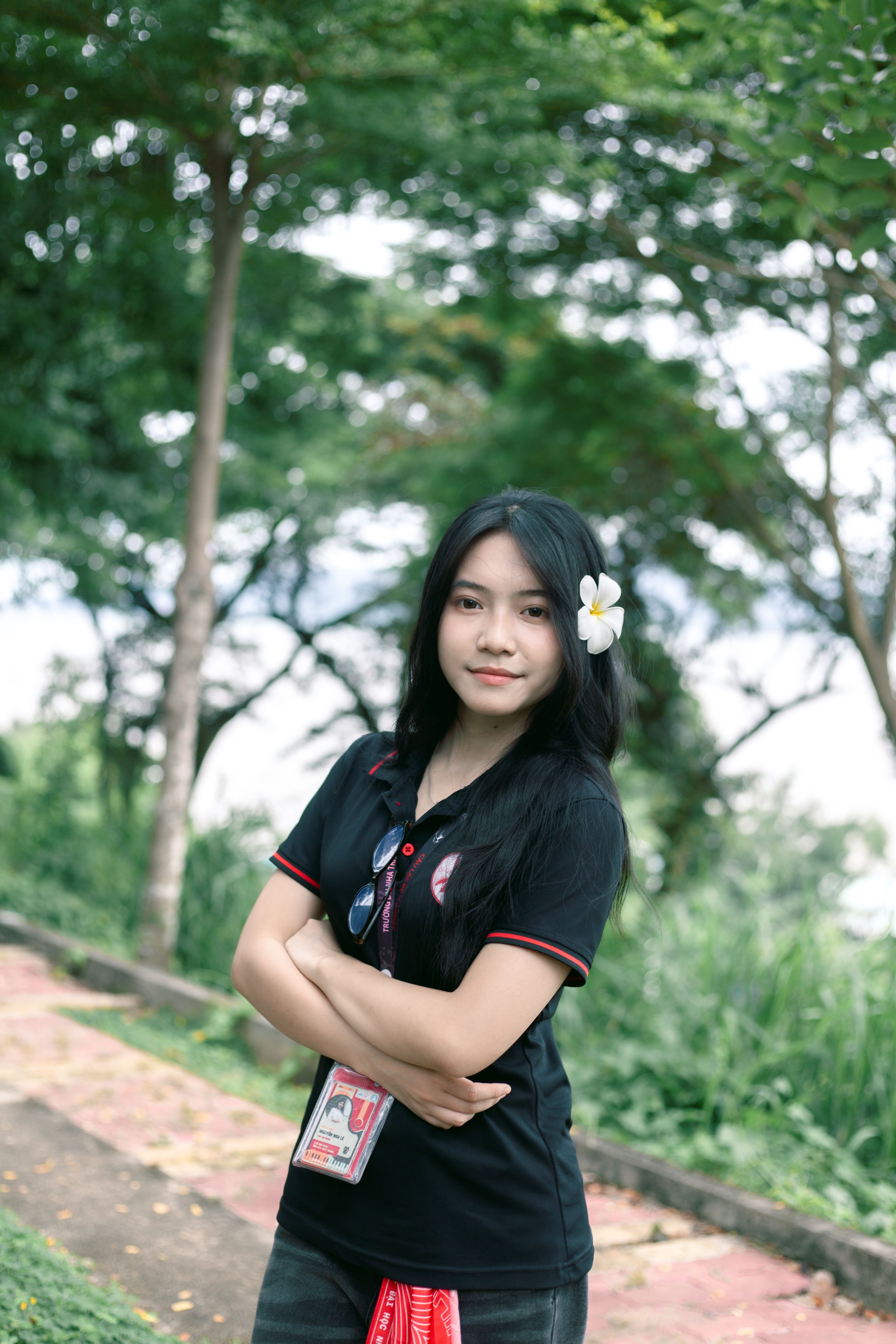 Young woman with flower in hair posing outdoors, surrounded by greenery.