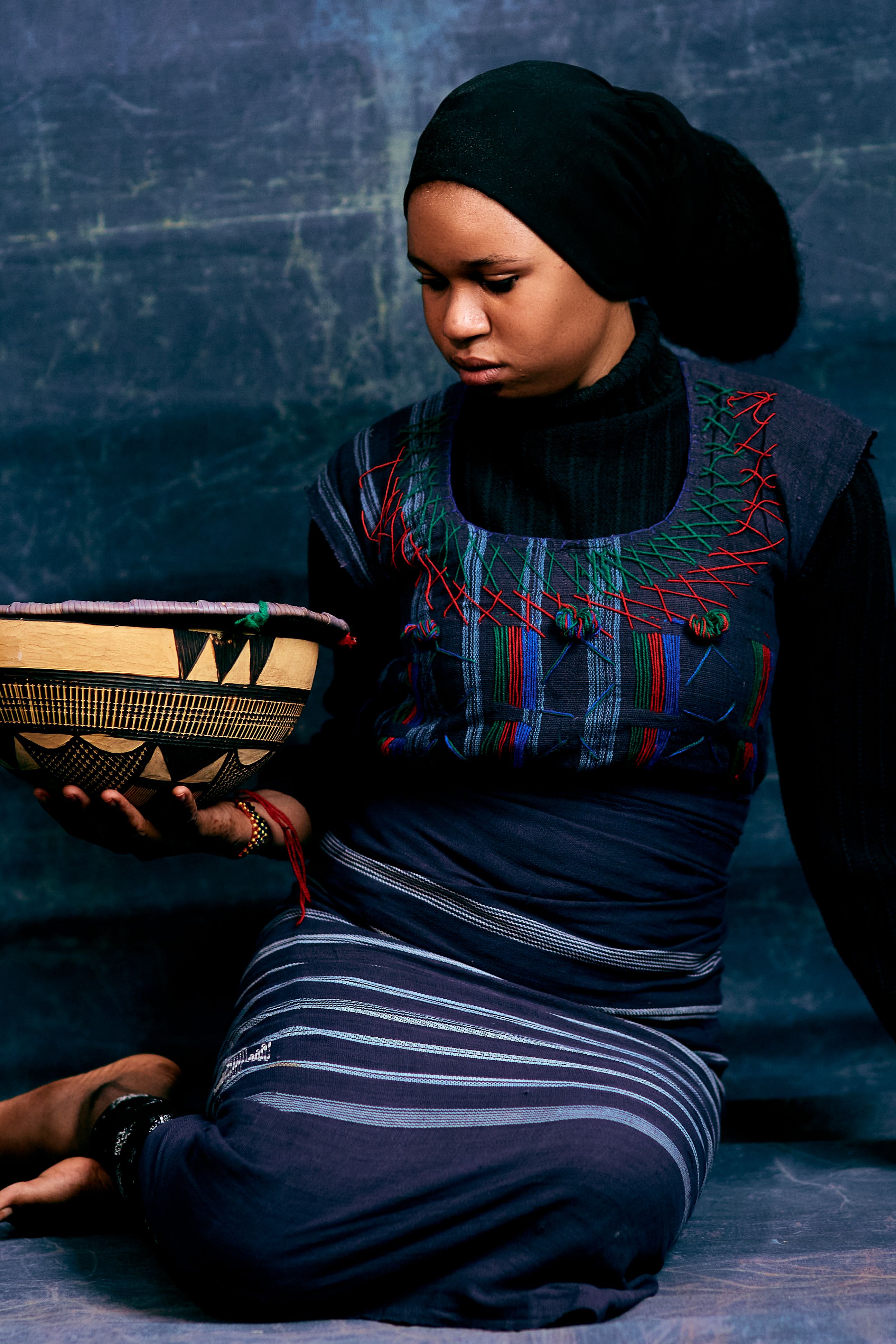 Woman in traditional attire holding African basket, cultural portrait.