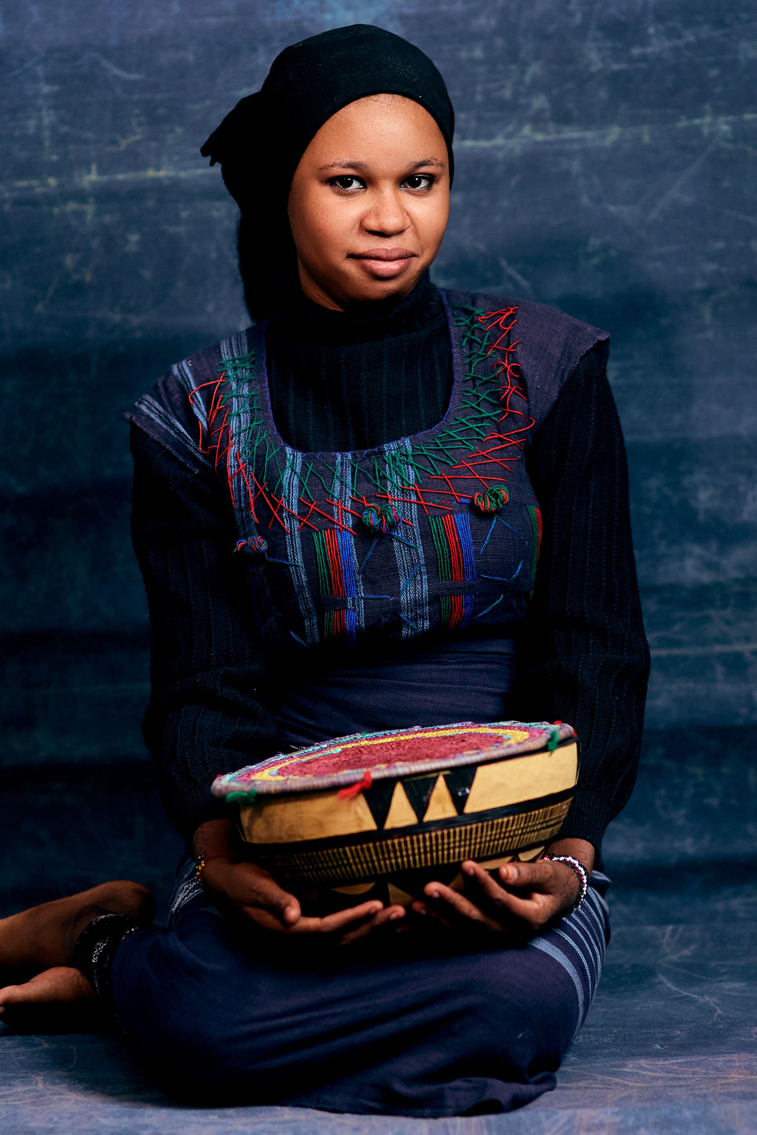 Woman dressed in ethnic attire holding a colorful traditional drum.