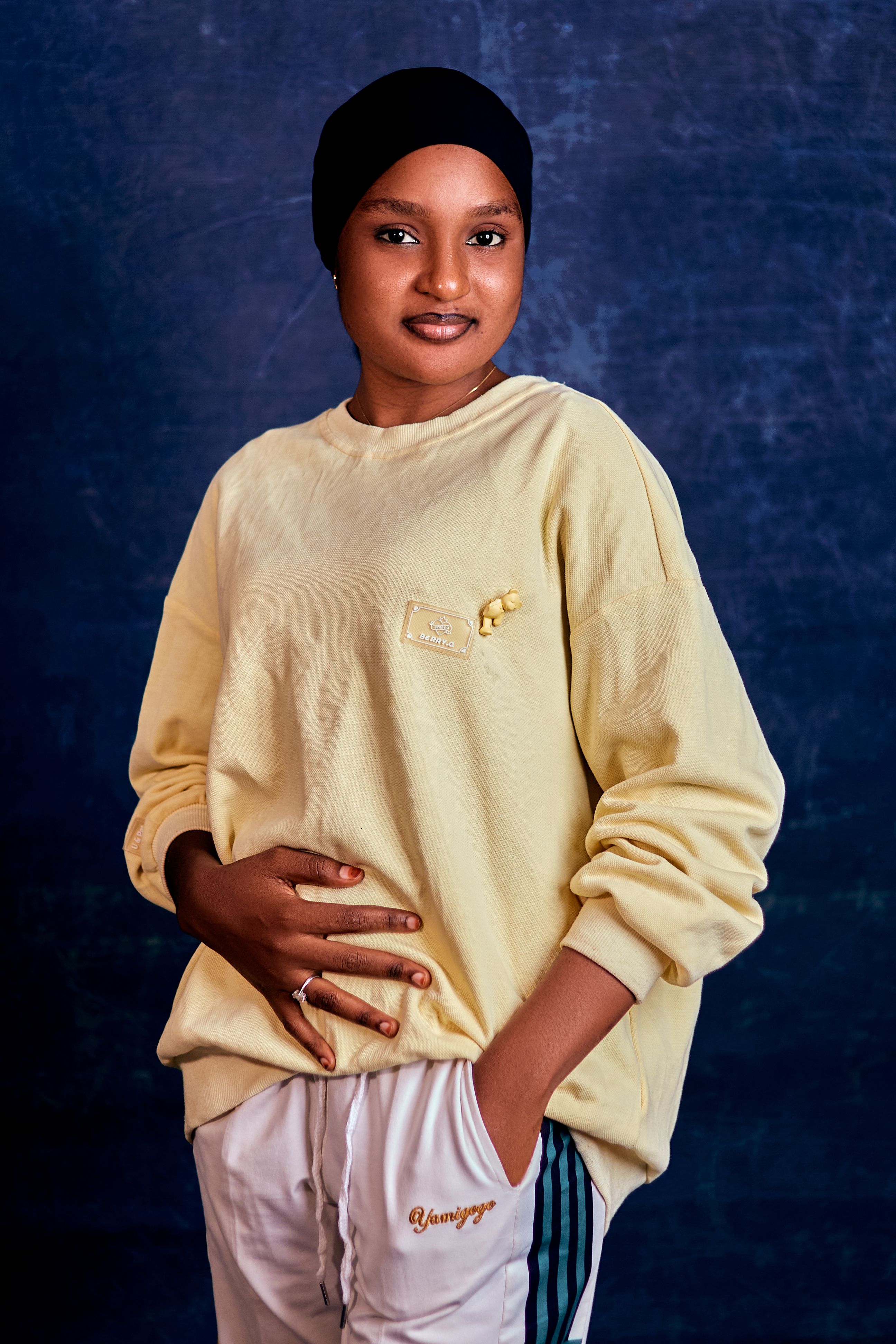 A charming portrait of a woman smiling confidently while wearing a yellow sweatshirt and white pants.