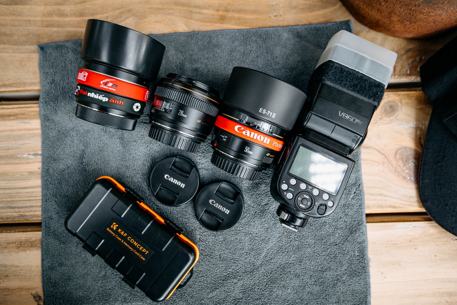 Flat lay of camera lenses, flash, and accessories on a wooden table.