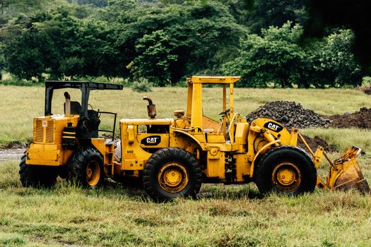 Yellow construction machinery in a green field surrounded by trees, showcasing industrial and natural contrast.