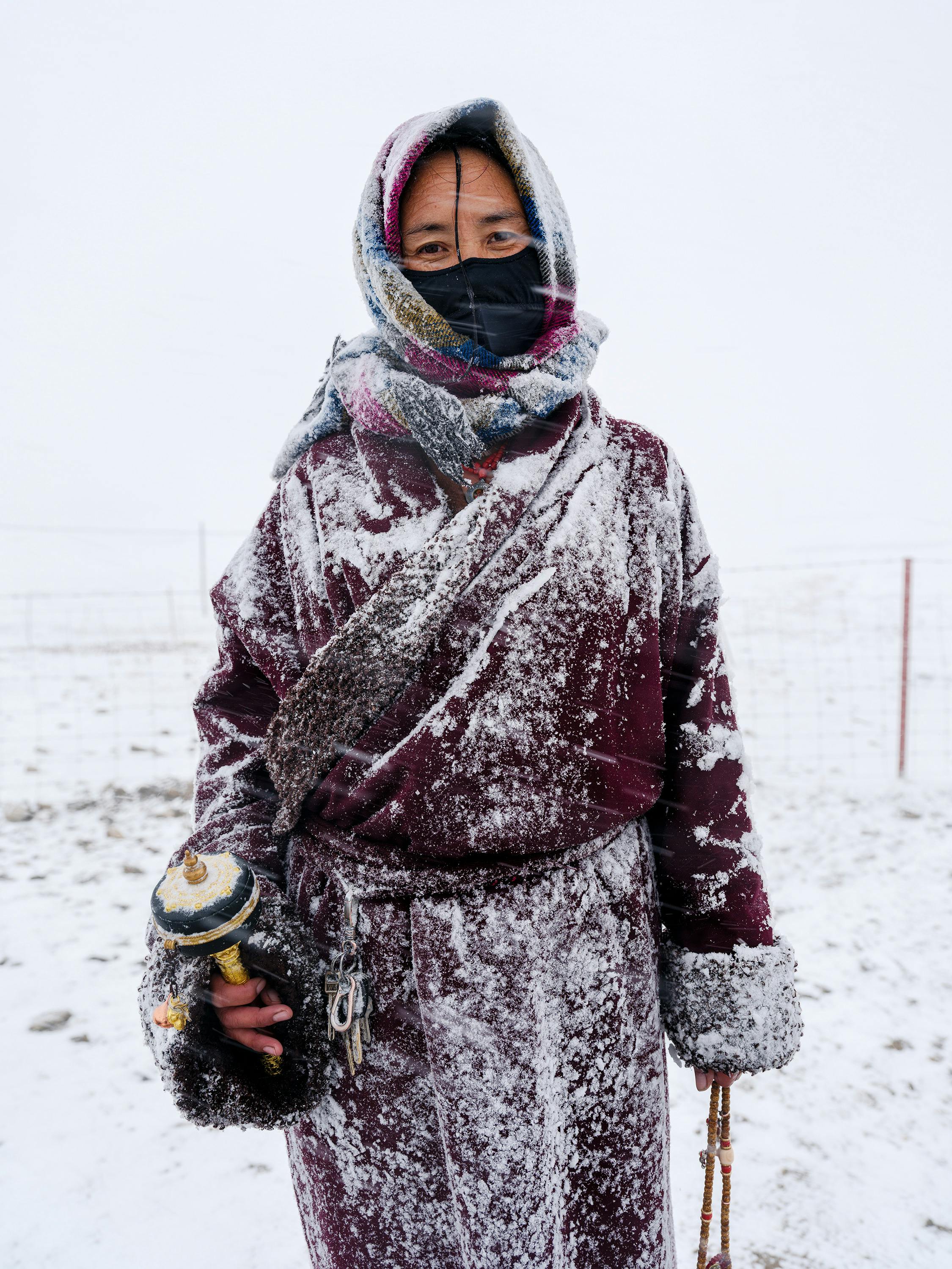 Individual dressed in warm clothing during a snowy winter day, holding a prayer wheel.