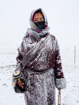 Individual dressed in warm clothing during a snowy winter day, holding a prayer wheel.