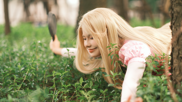 Blonde woman smiling while lying on grass in a forest enjoying nature.