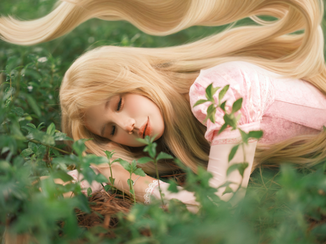 Blonde woman in a pink dress lying peacefully among green foliage.