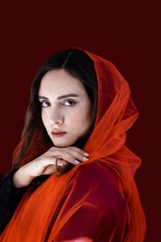 Stunning portrait of a woman in an orange veil with a dark red background.