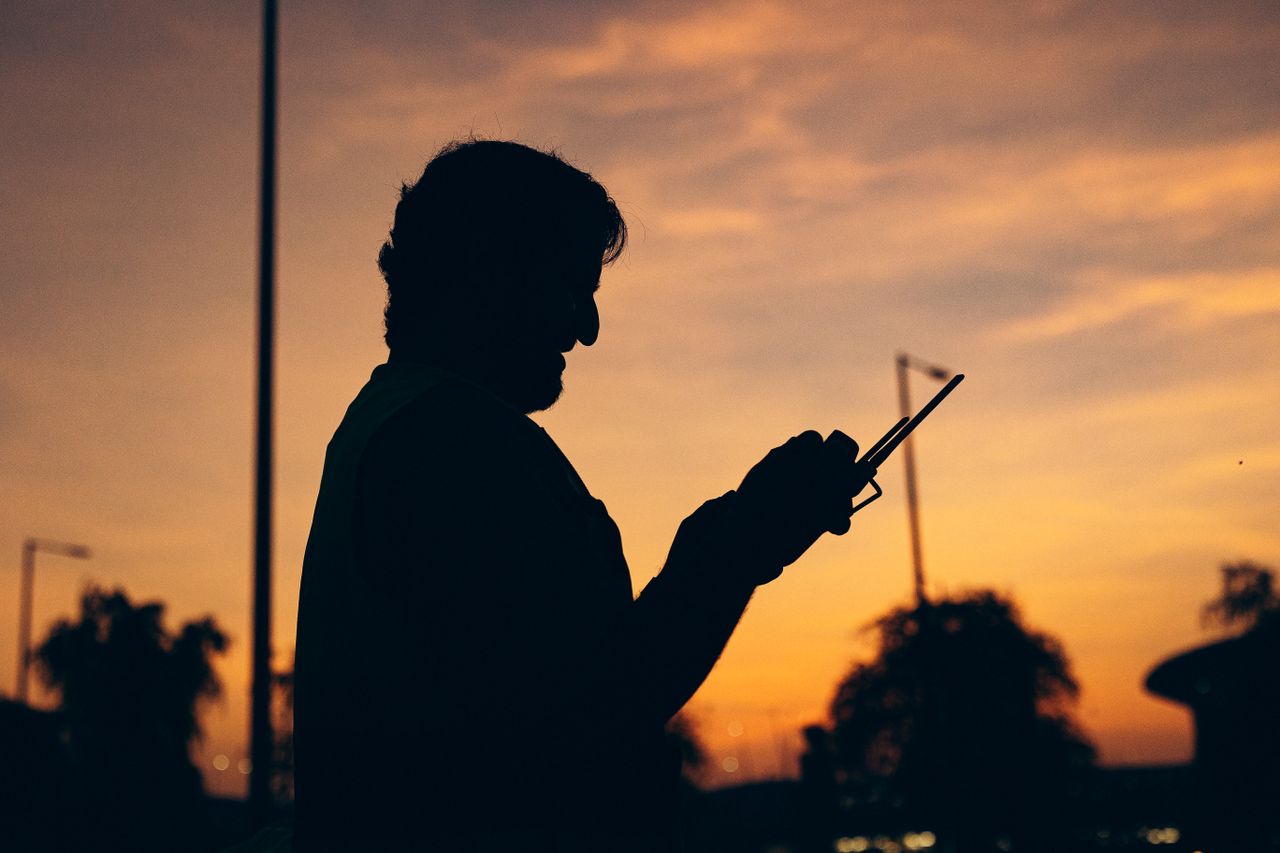silhouette of a person holding a smartphone against a vibrant sunset i