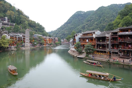 A tranquil view of Fenghuang Ancient Town showcasing traditional wooden houses and boats on the river.