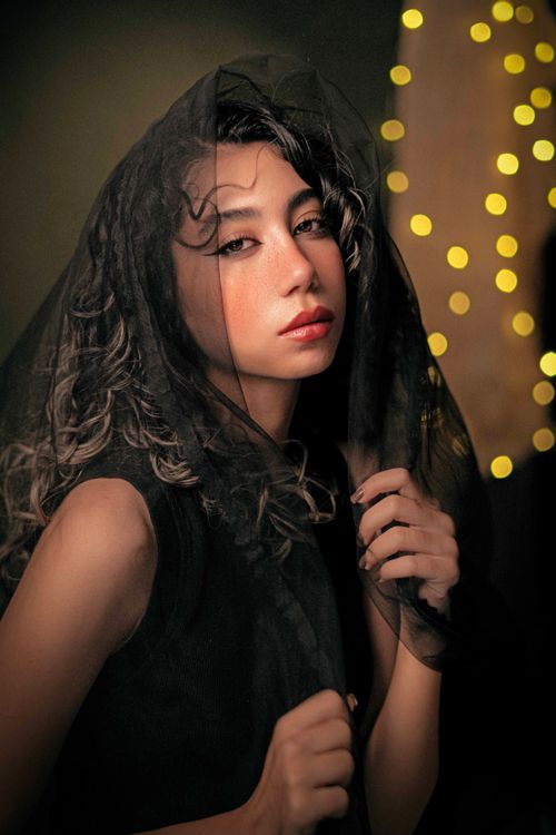 Free Emotive portrait of a woman covered in a veil with glowing bokeh lights in the background. Stock Photo