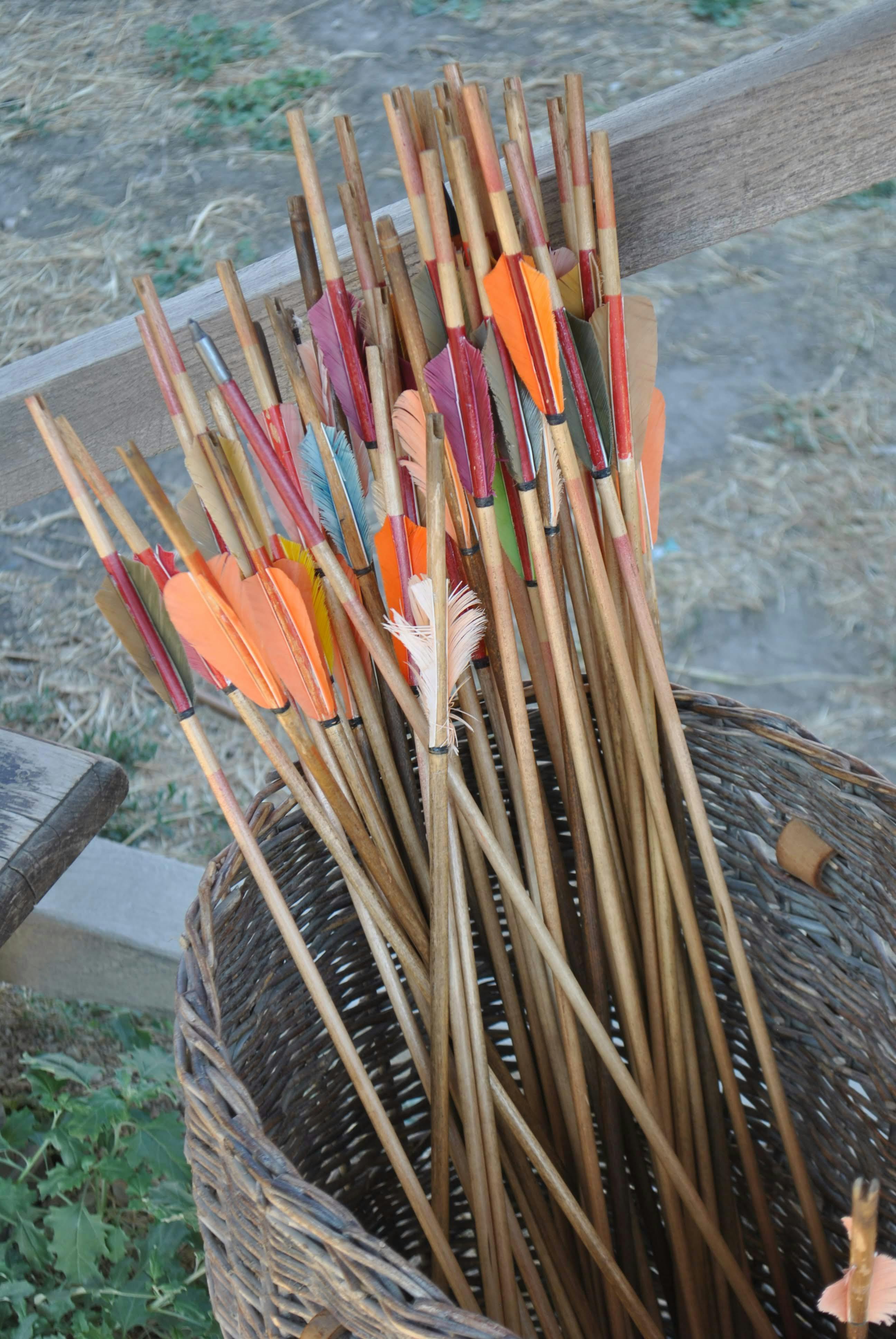 A basket full of colorful, handcrafted wooden arrows displayed outdoors.