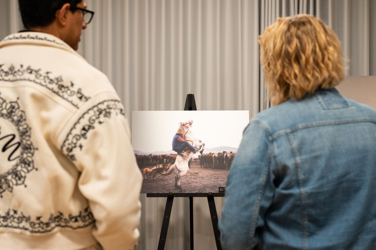 two adults admire a photo of a rider on a horse at an indoor exhibitio