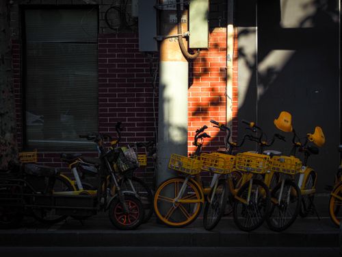 Free Row of yellow bikes parked by a brick wall, casting shadows during daylight. Stock Photo