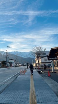 A person walks along a street in Tokyo with snow-capped mountains under a clear blue sky.
