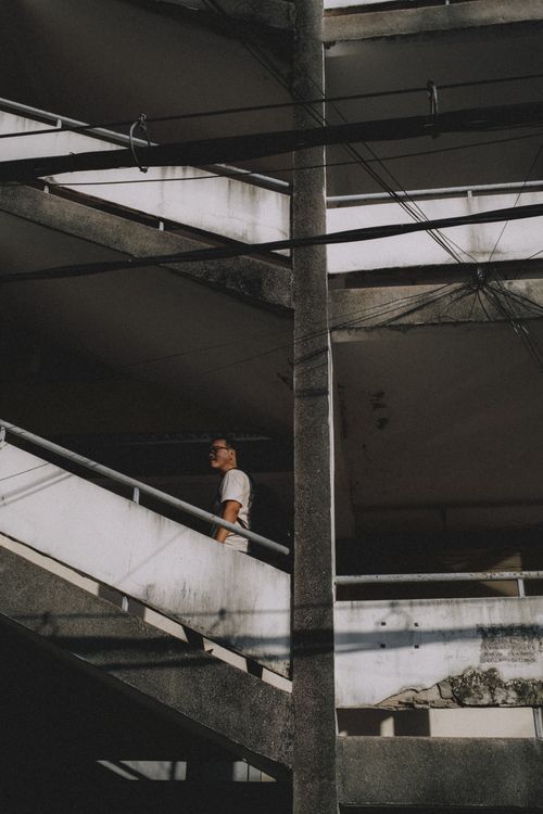 Free A person stands thoughtfully on a shadowed urban staircase. Stock Photo