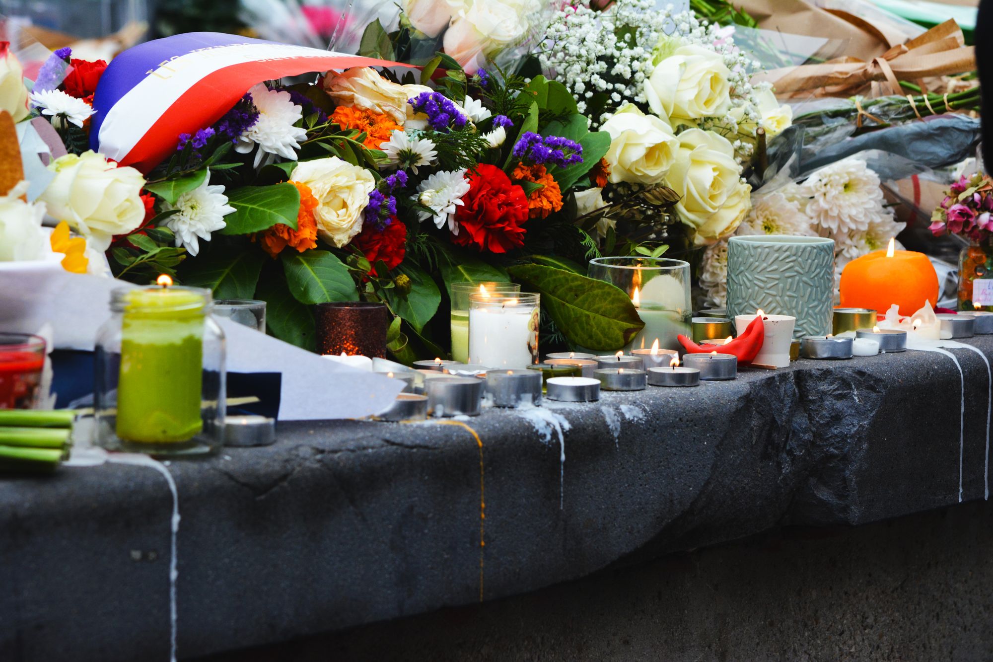 Velas encendidas y flores dejadas sobre una acera en un memorial improvisado