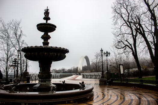 Foggy morning at Friendship of Nations Arch, Kyiv, with silhouette of trees and fountain.