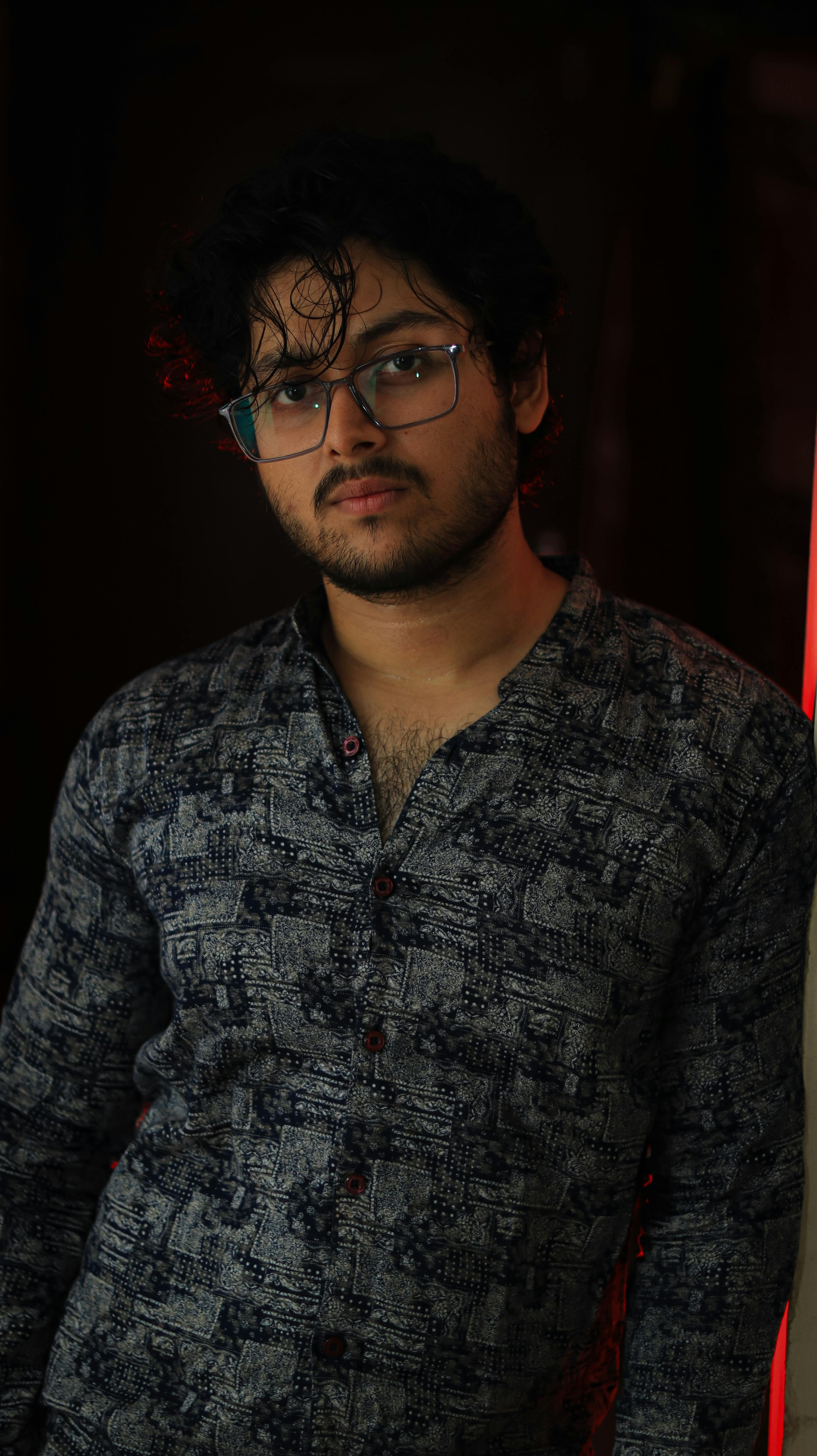 Portrait of a man in casual attire with glasses, exuding a cool attitude in an indoor setting.