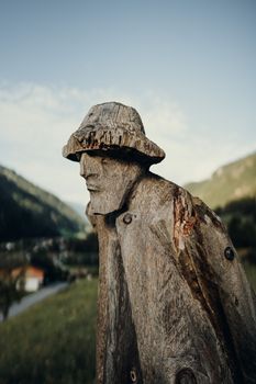 A rustic wooden sculpture of a man outdoors with a scenic mountainous landscape.