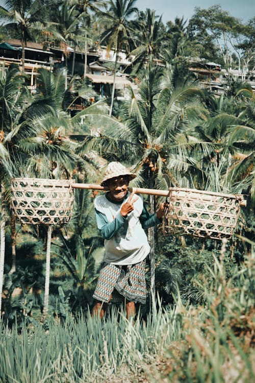 Person in White and Green Long Sleeves Shirt and Brown Straw Hat Carrying Brown Woven Basket