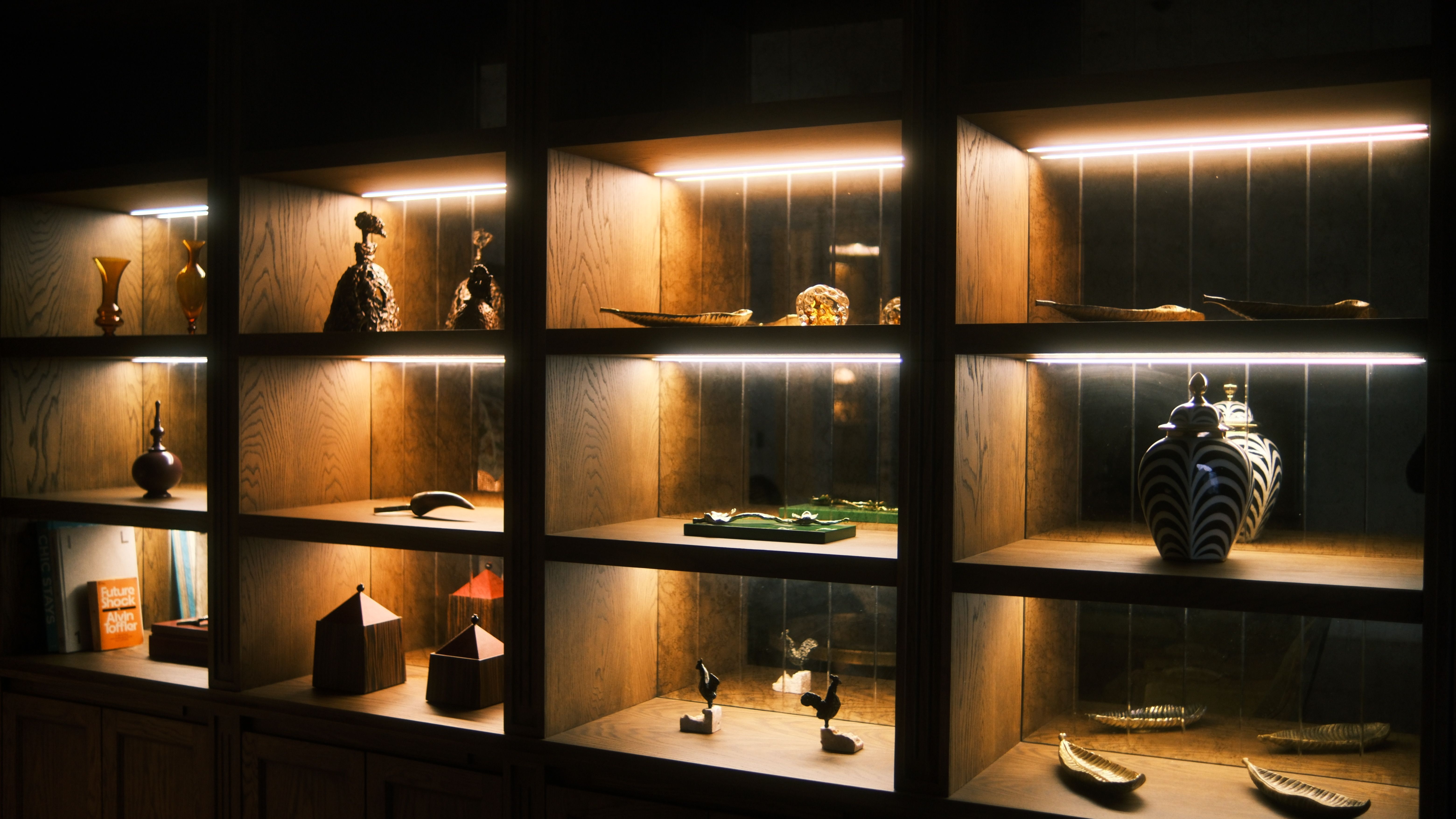 Free Wooden display shelves with artistic ceramics and sculptures elegantly lit for a warm ambiance. Stock Photo