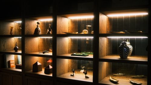 Free Wooden display shelves with artistic ceramics and sculptures elegantly lit for a warm ambiance. Stock Photo