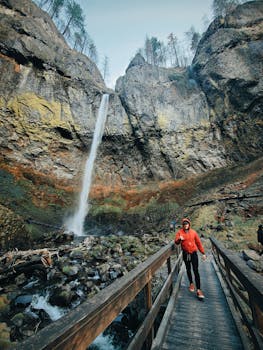 一名徒步旅行者穿着红色夹克，穿过人行天桥，背景是一座壮观的瀑布