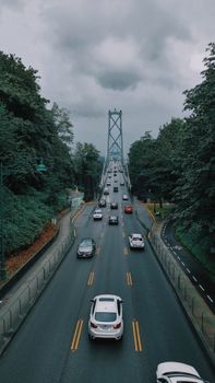 High angle of paved asphalt route leading to bridge among green trees under gloomy sky