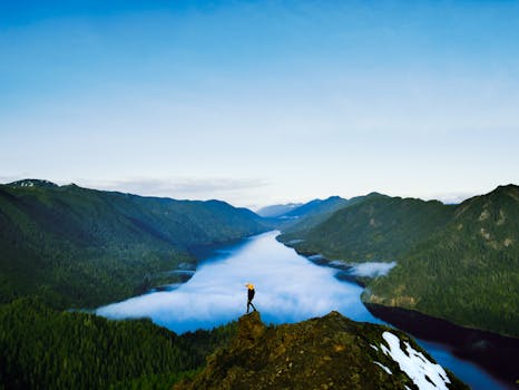 一位孤独的徒步旅行者站在山峰上，俯瞰着山谷与河流的壮丽景色