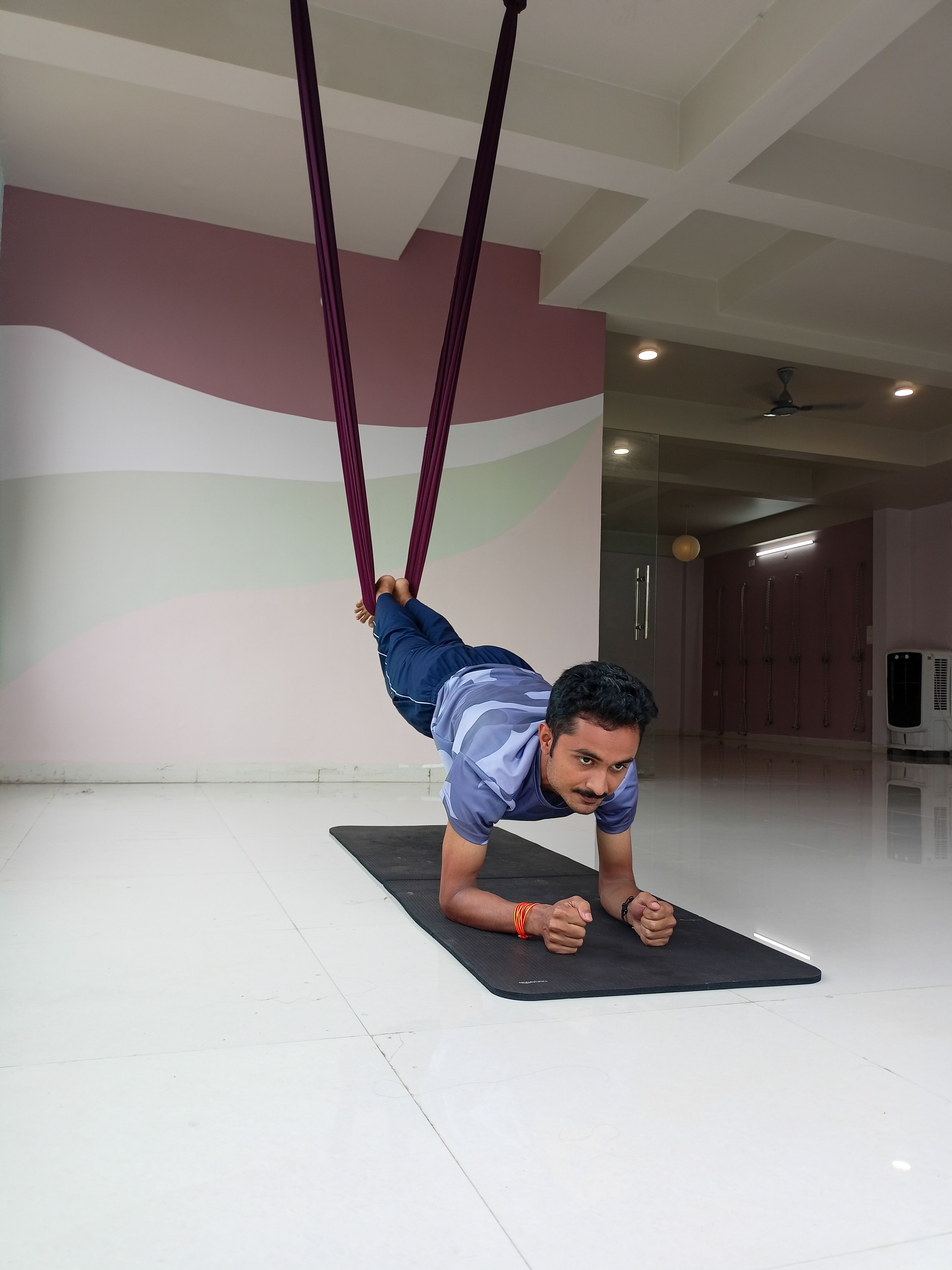 An adult man exercises with aerial yoga straps indoors, promoting fitness and flexibility.