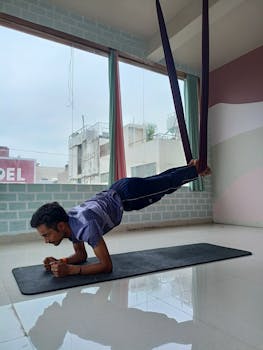 A man performs aerial yoga inside a bright room, showcasing strength and balance.