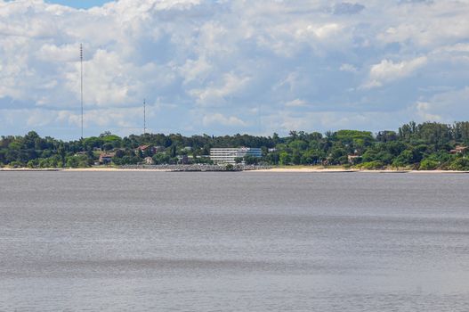 Picturesque view of Colonia del Sacramento's coastline from across the river, under a cloudy sky.