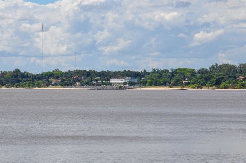 Free Picturesque view of Colonia del Sacramento's coastline from across the river, under a cloudy sky. Stock Photo