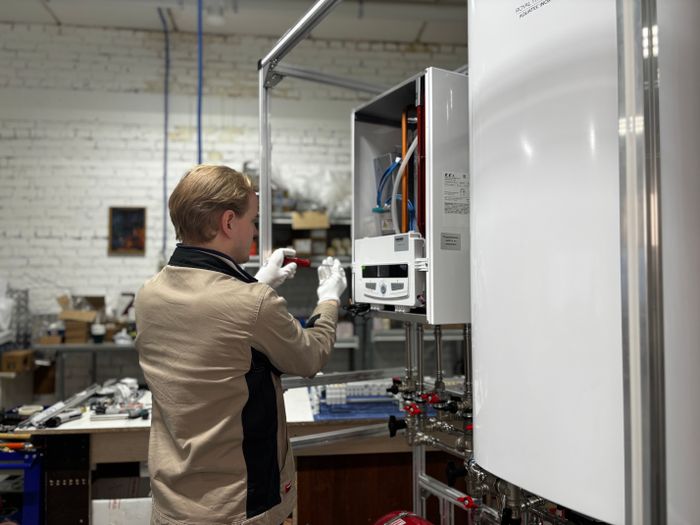 Technician servicing a wall-mounted water heater with the casing opened