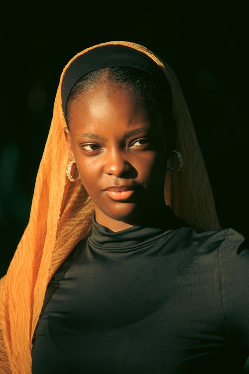 Free Elegant portrait of a woman wearing a golden headscarf, bathed in warm sunlight, showcasing thoughtful expression. Stock Photo