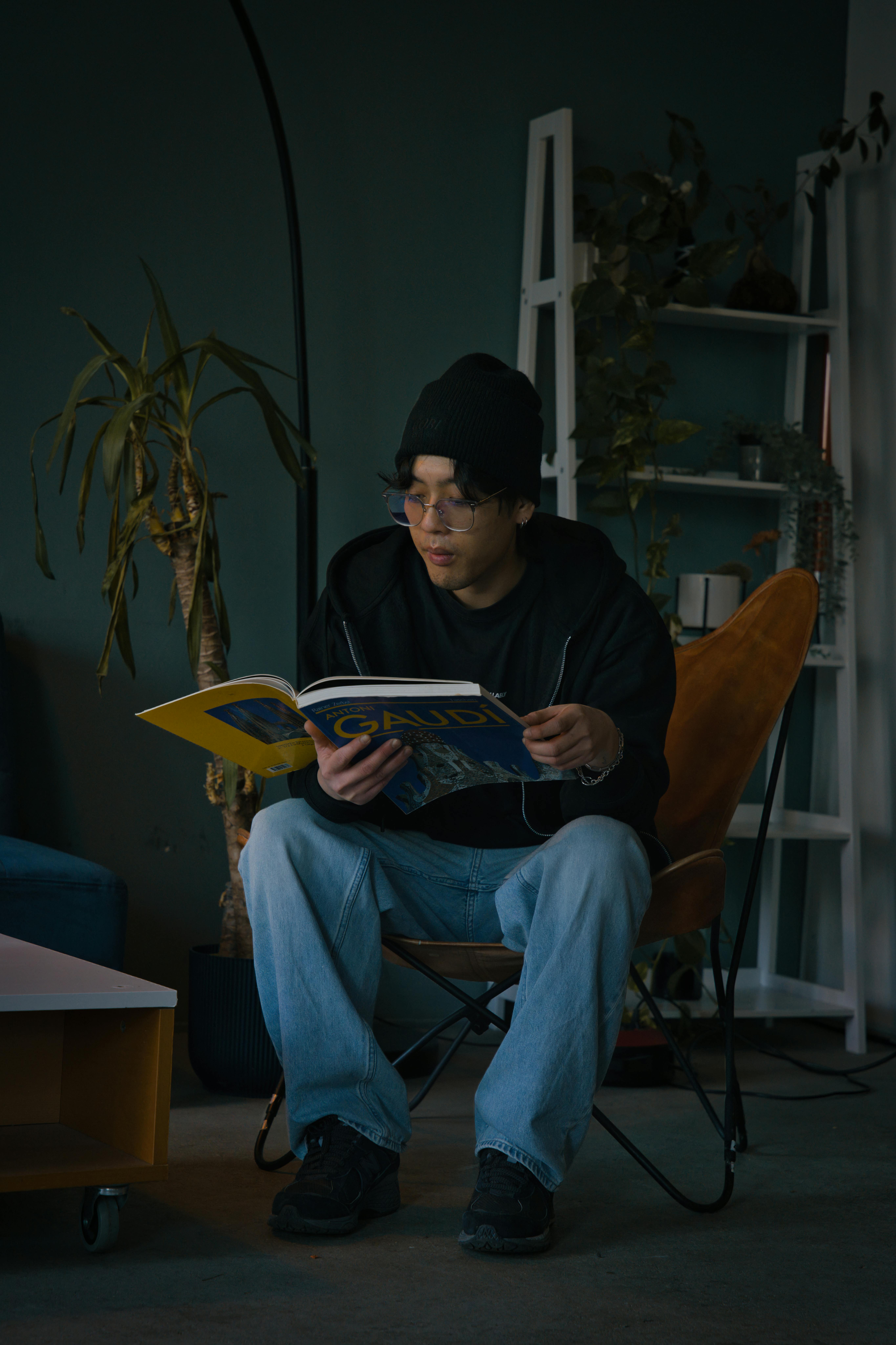 Gratis En ung mann sitter i en stol innendørs og leser et blad i koselige omgivelser. Arkivbilde