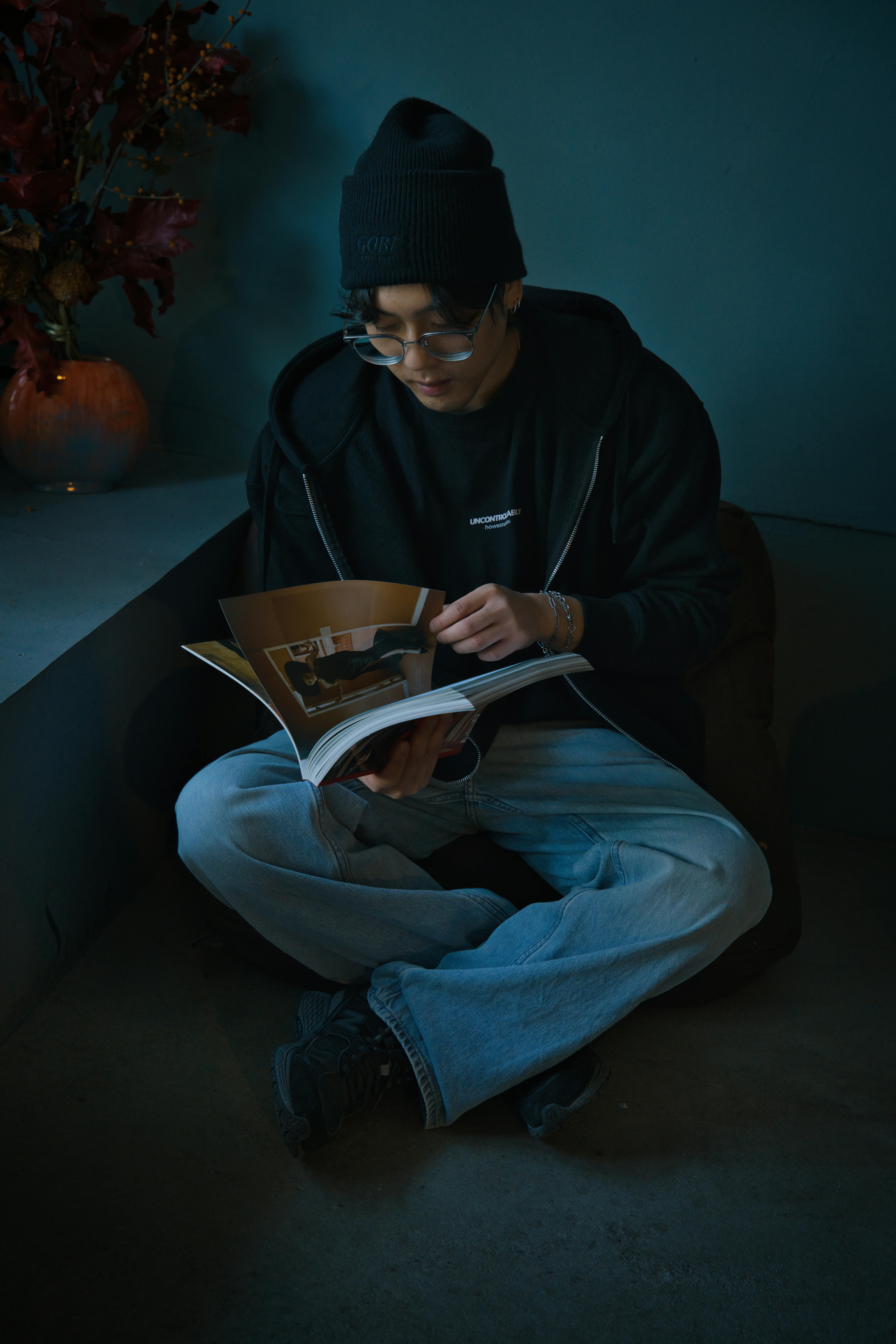 grátis Um jovem está sentado dentro de casa, lendo uma revista em um canto aconchegante. Perfeito para temas de estilo de vida e relaxamento. Foto profissional